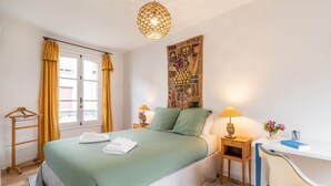 Un dormitorio con cama, escritorio, silla, lámpara colgante y un tapiz en la pared.