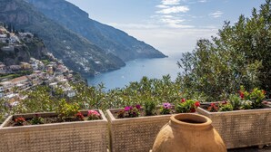 A coastal town with terraced houses, a large clay pot, and flower planters in the foreground. - Rosa House (Positano)