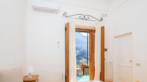 A bedroom with a bed, a nightstand, a window with curtains, and a view of mountains. - Rosa House (Positano)