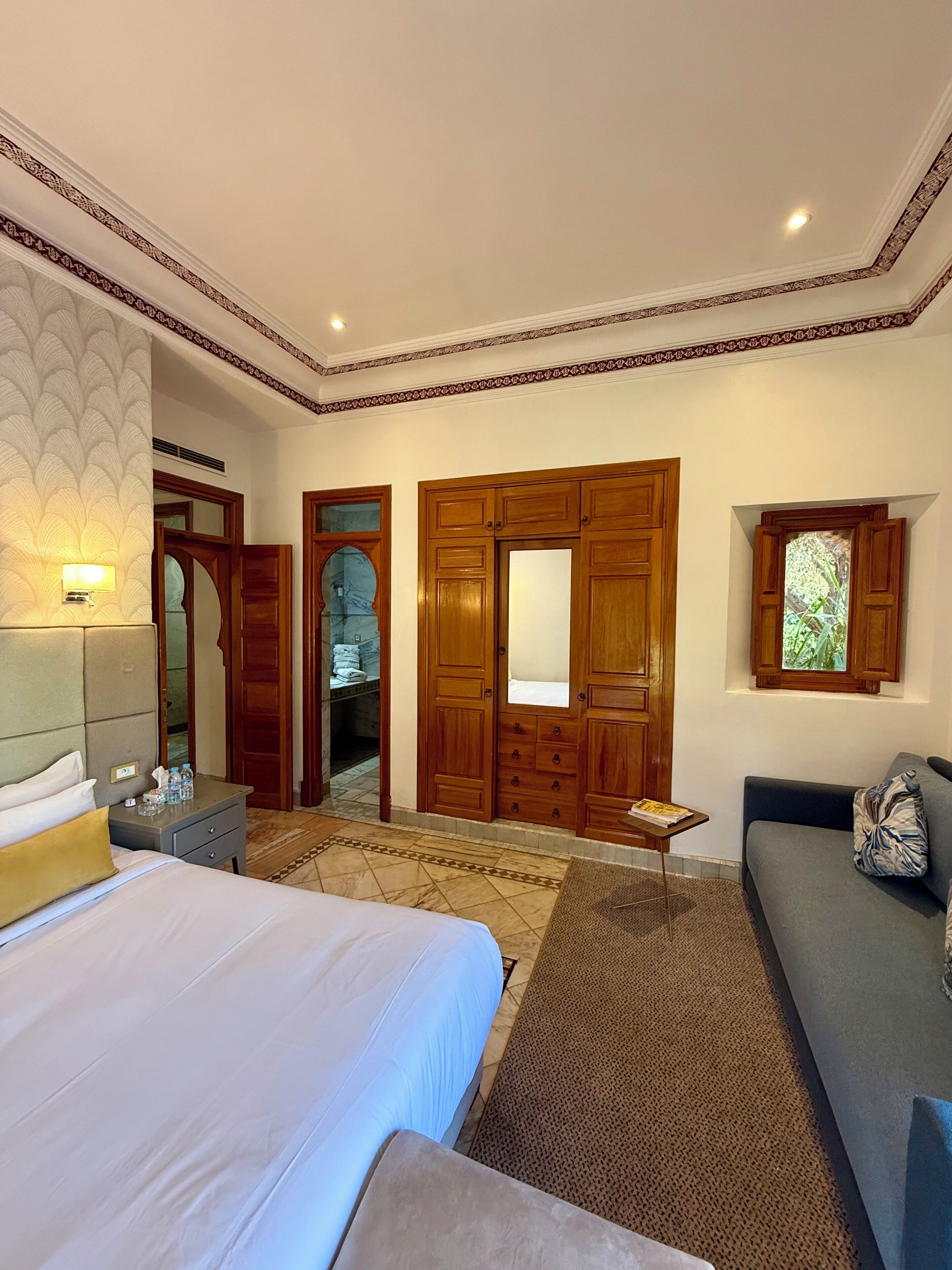 A hotel room with a large bed, a sofa, a wooden wardrobe, and a mirror.
