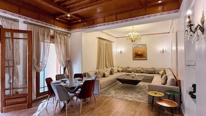 Amplia sala de estar con techo de madera, un gran sofá, una zona de comedor con sillas y una mesa, y una araña.