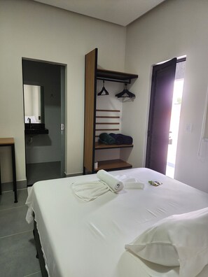 A hotel room with a bed, a bedside table, a mirror, a wardrobe with hanging space, and a door leading to another room. - Friper Hotel (Jaraguá)