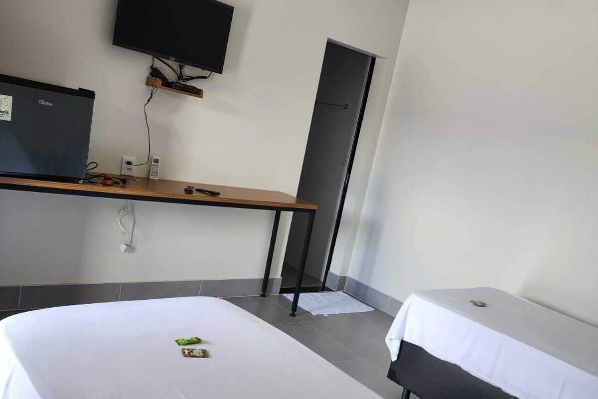A hotel room with two beds, a desk with a computer, a flat-screen TV, and a wardrobe.