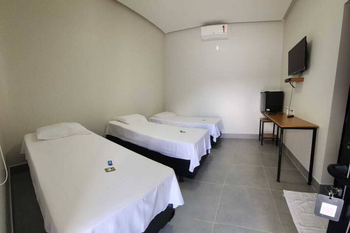 A hotel room with three single beds, a desk, a chair, a television, and an air conditioning unit.