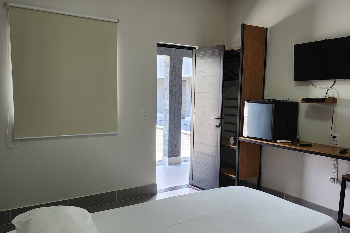 A hotel room with a bed, a TV mounted on the wall, and a door leading to an outdoor area.