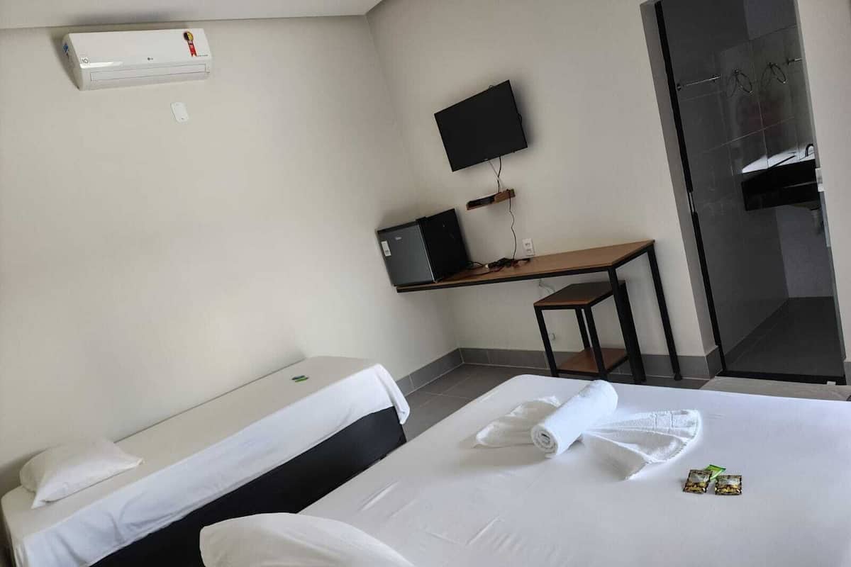 A hotel room with two beds, a desk with a computer, a TV, and a shower area.