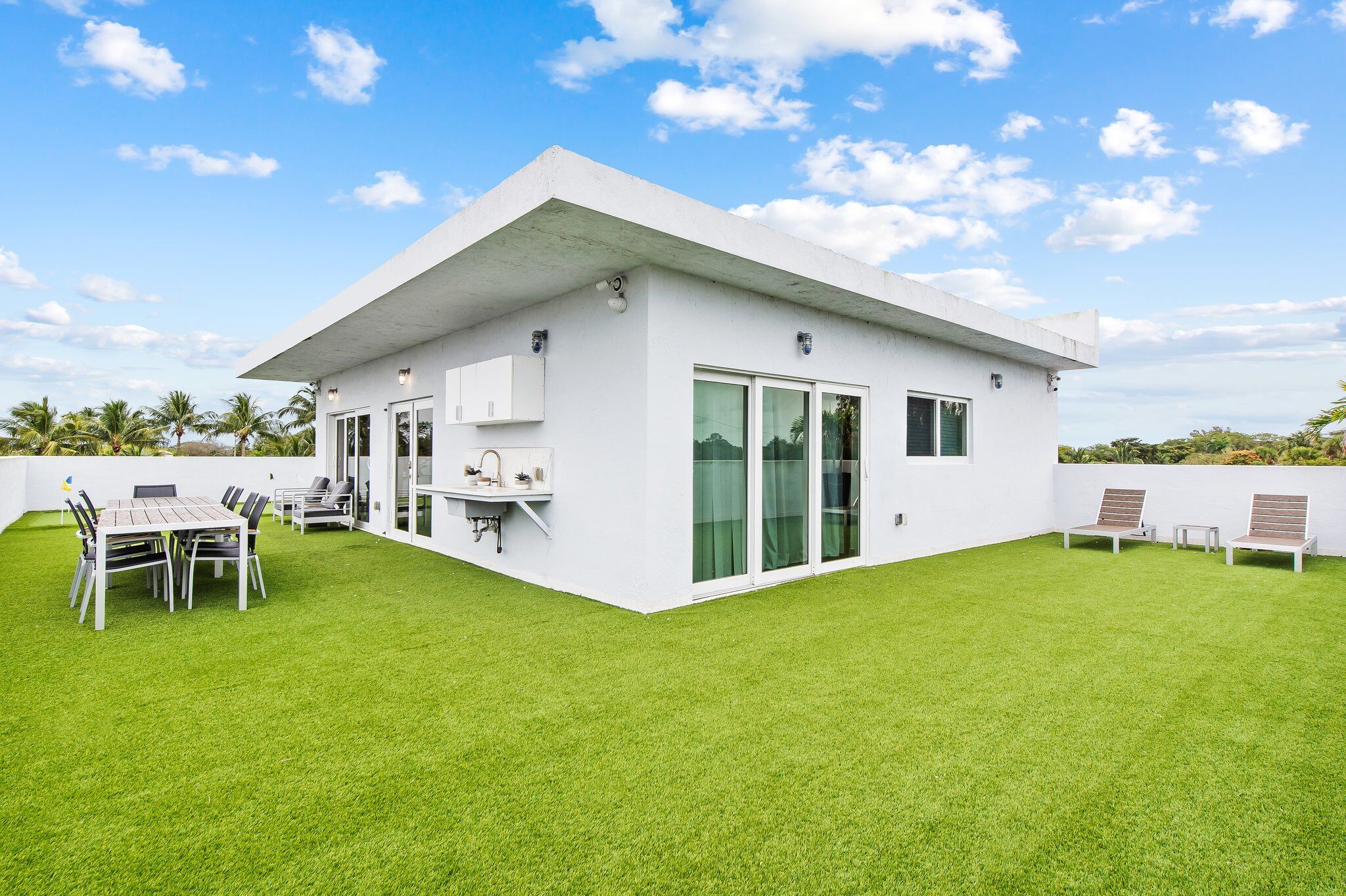 A modern white house with a flat roof, large sliding glass doors, and a well-maintained lawn.