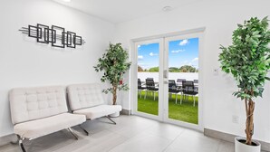 Ein moderner Wartebereich mit einem weißen Sofa, zwei Blumentöpfen und einer Glastür, die zu einem Außenbereich führt.