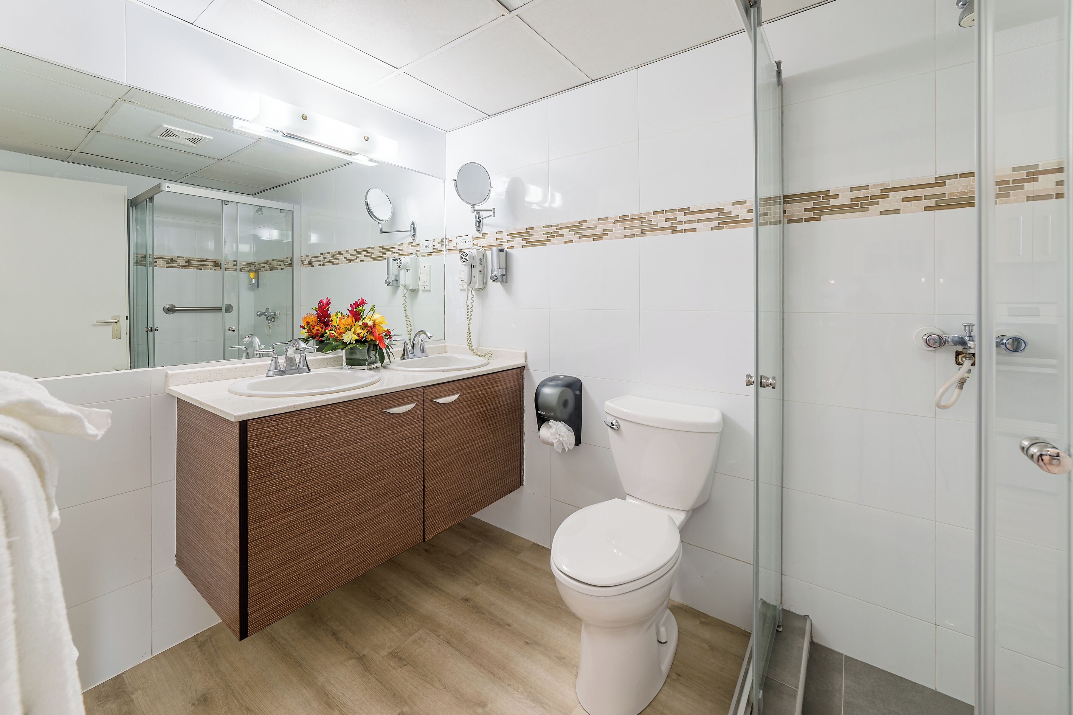 Ein modernes Badezimmer mit Duschkabine aus Glas, einem Holzwaschtisch, einer Toilette und einem Spiegel mit Handtuchhalter.