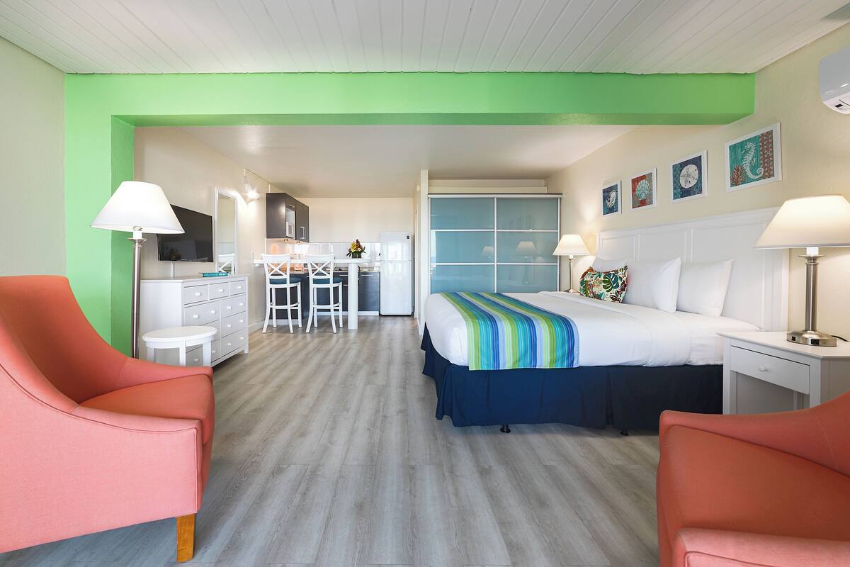 Una habitación de hotel con cama, dos sillas, escritorio, mesita y kitchenette.