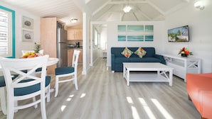 A spacious living area with a blue sofa, white coffee table, and a dining table with chairs. A kitchen is visible in the background, and there are framed pictures on the walls. - La Vista Hotel (Simpson Bay)
