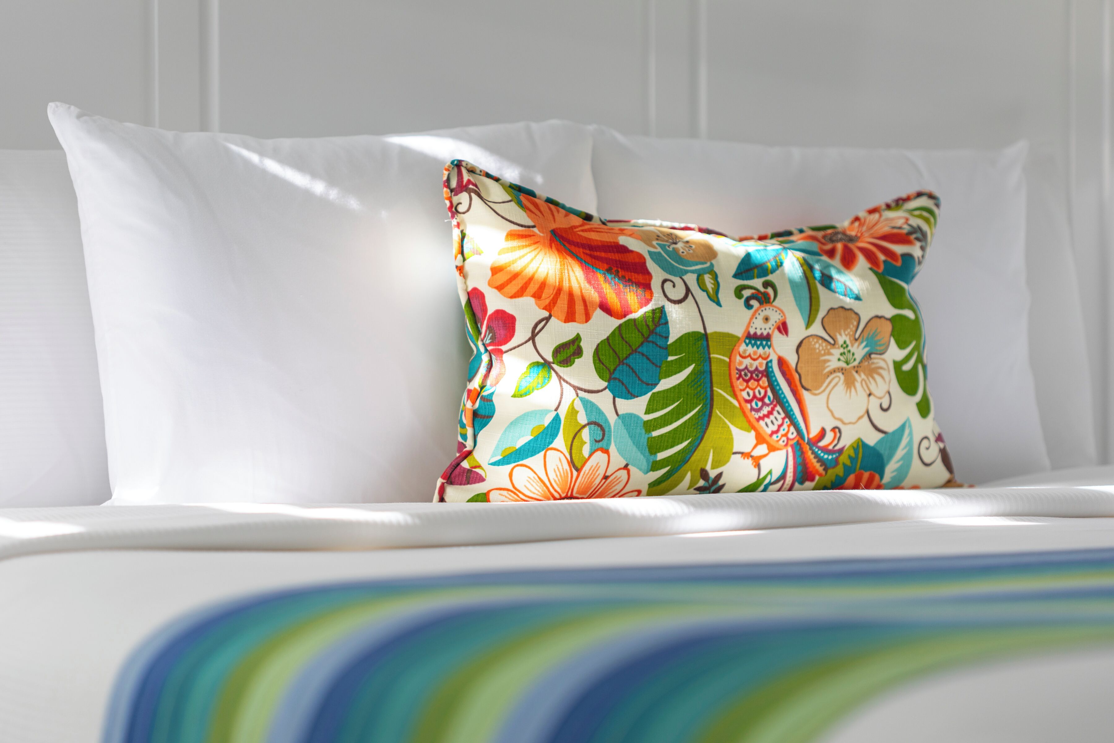 Een bed met witte lakens en een kleurrijk, bloemenprint kussen.