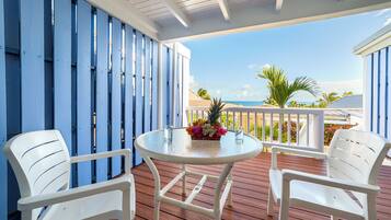A covered outdoor area with a round table and two white chairs, a blue fence, and a view of the ocean.