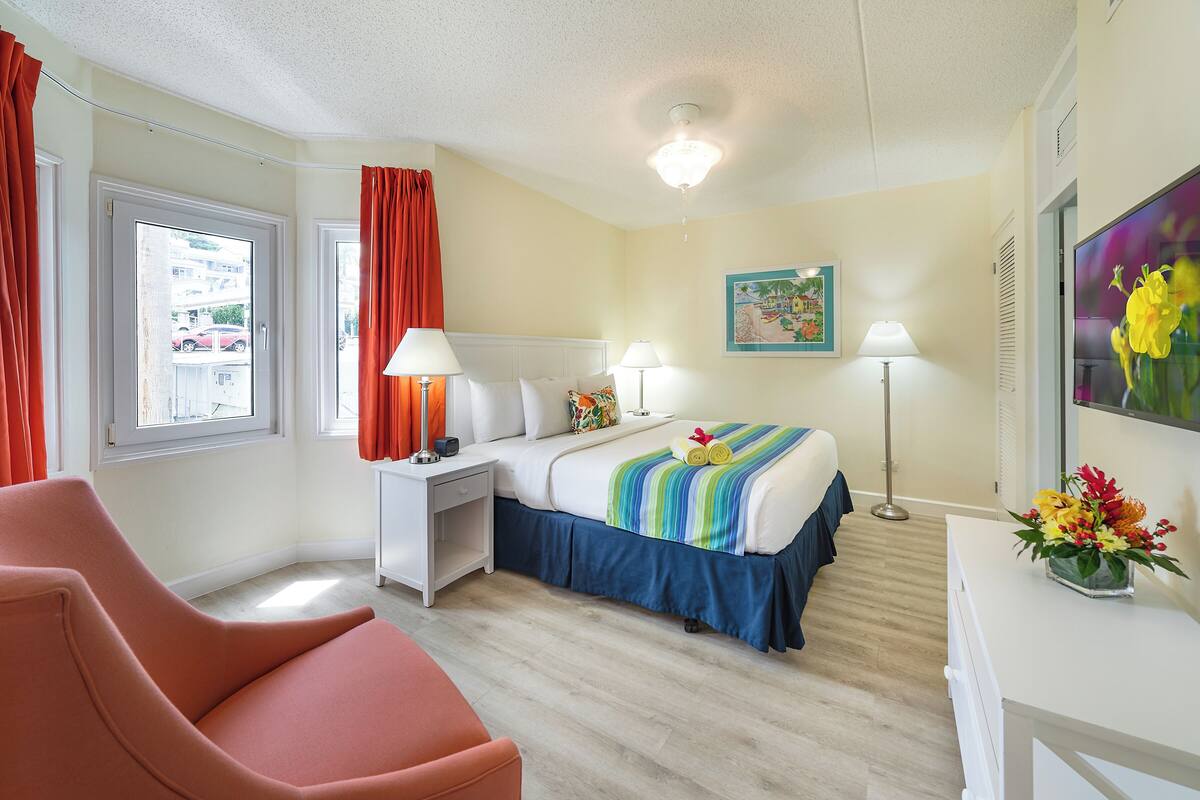 Una habitación de hotel con cama, mesitas de noche, una silla, un escritorio y una ventana con cortinas.