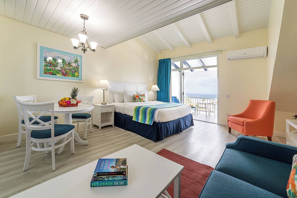 Habitación de hotel con cama, escritorio, silla, mesa con libros y vista al exterior.