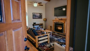 A cozy living room with a fireplace, a ceiling fan, and a television mounted on the wall.