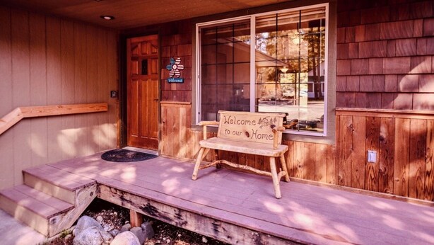A wooden cabin with a wooden bench outside, a welcome sign, and a door with a sign above it.