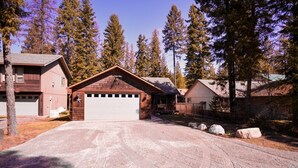 A two-story house with a garage, surrounded by trees and a gravel driveway.