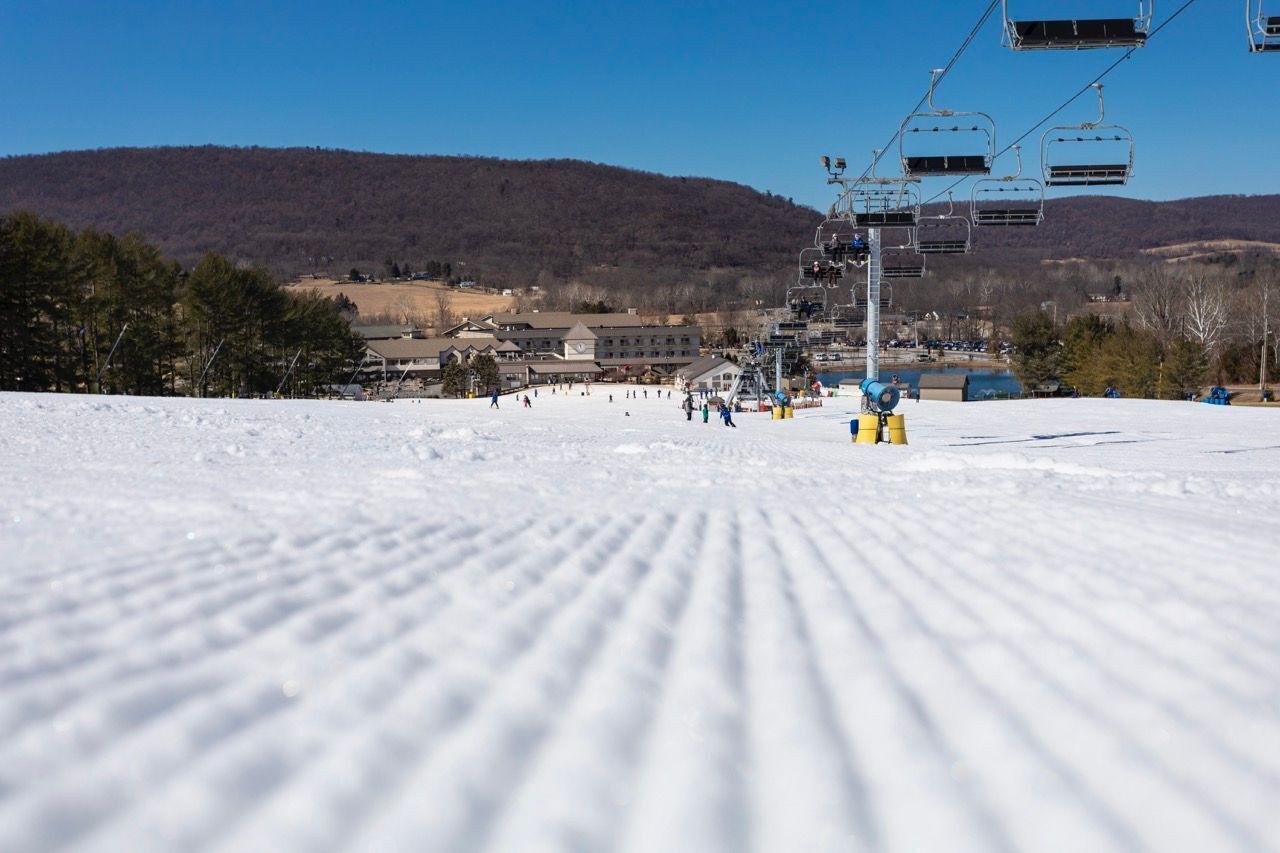 A ski slope with a ski lift, buildings in the background, and a clear sky.