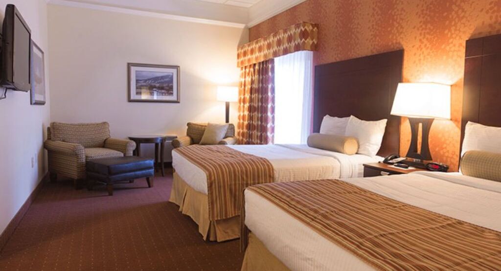A hotel room with two beds, a sofa, a small table, and a TV.