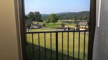 A view from a balcony overlooking a golf course with a pond, trees, and distant hills.