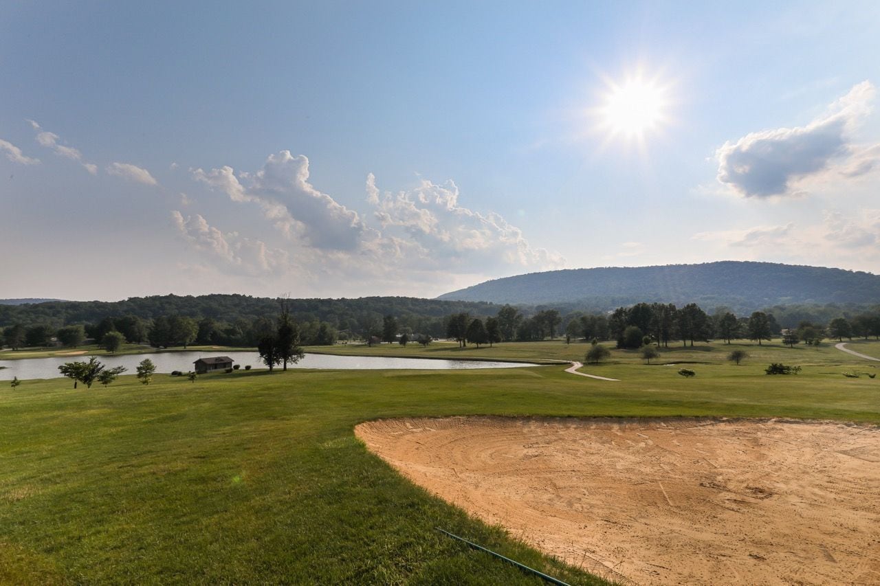 A golf course with a pond, trees, and a hill in the background.