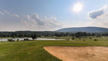 A golf course with a pond, trees, and a hill in the background.