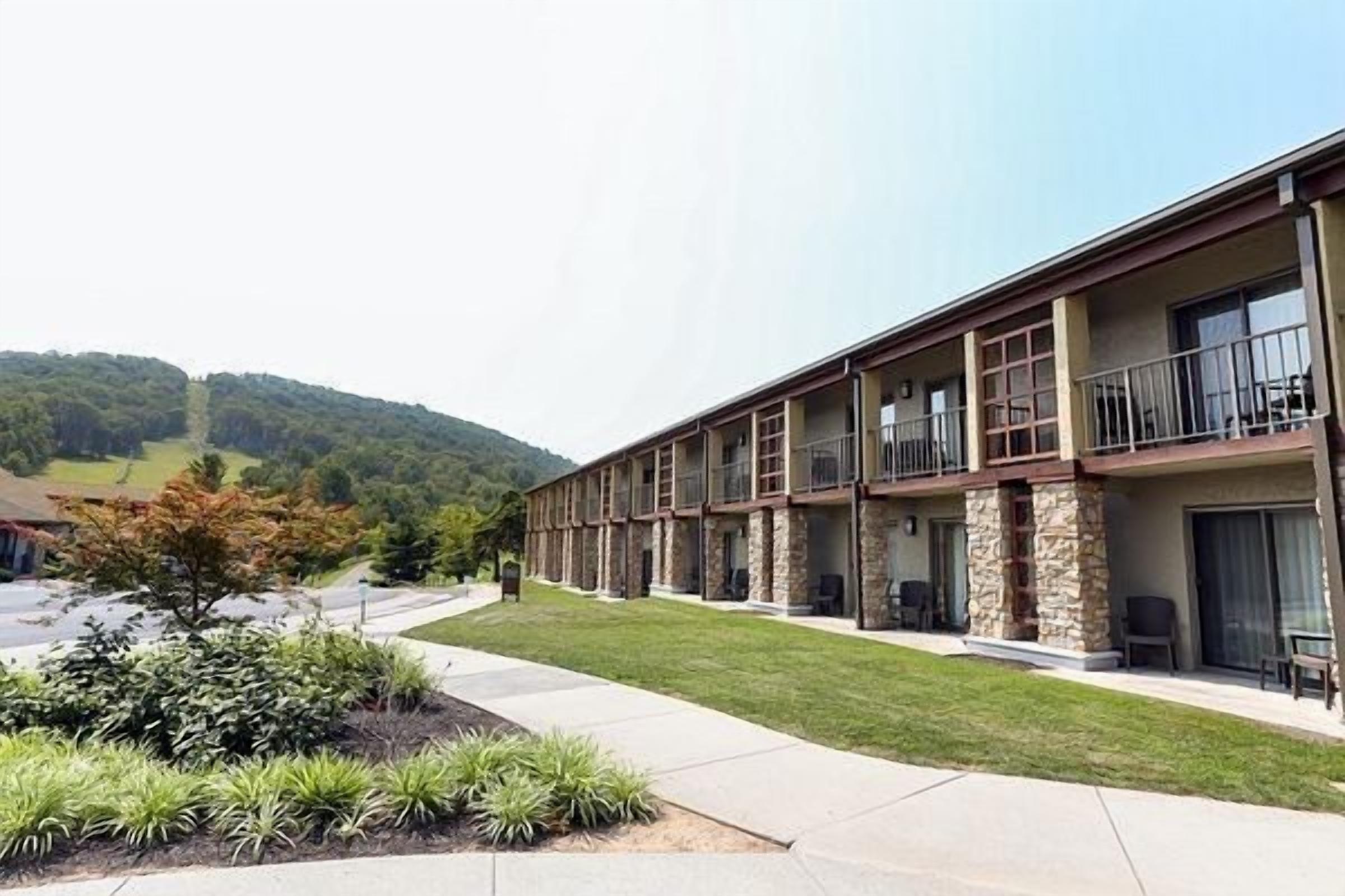Un hotel a più piani con tetto piatto, balconi e un giardino antistante curato.
