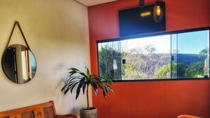 A room with a wooden bench, a potted plant, a large window with a view, and a wall-mounted mirror. - Pousada Lobo Guará (São João Batista do Glória)