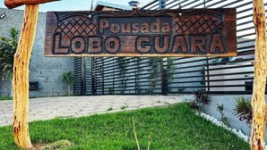 A wooden sign with the text 'Pousada Lobo Guara' mounted on a simple wooden structure. - Pousada Lobo Guará (São João Batista do Glória)
