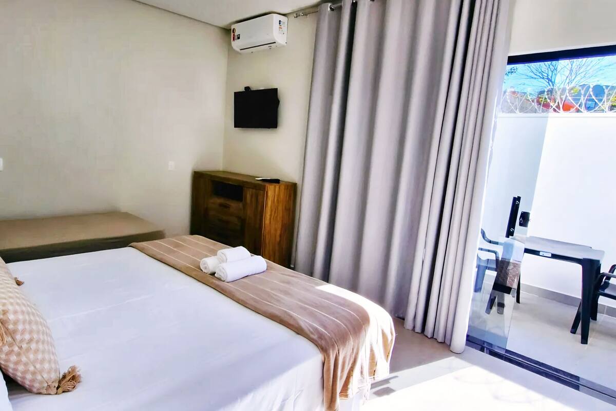 Habitación de hotel con cama, mesita de noche de madera, televisor y vistas al exterior.