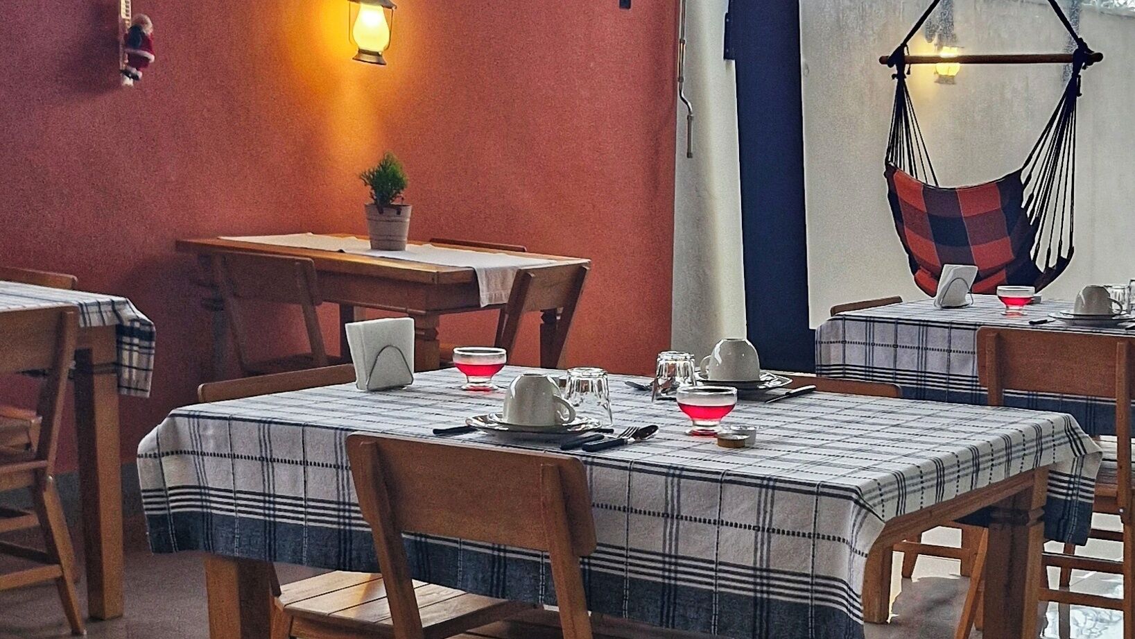 A dining area with tables set for two, featuring plaid tablecloths and wooden chairs.