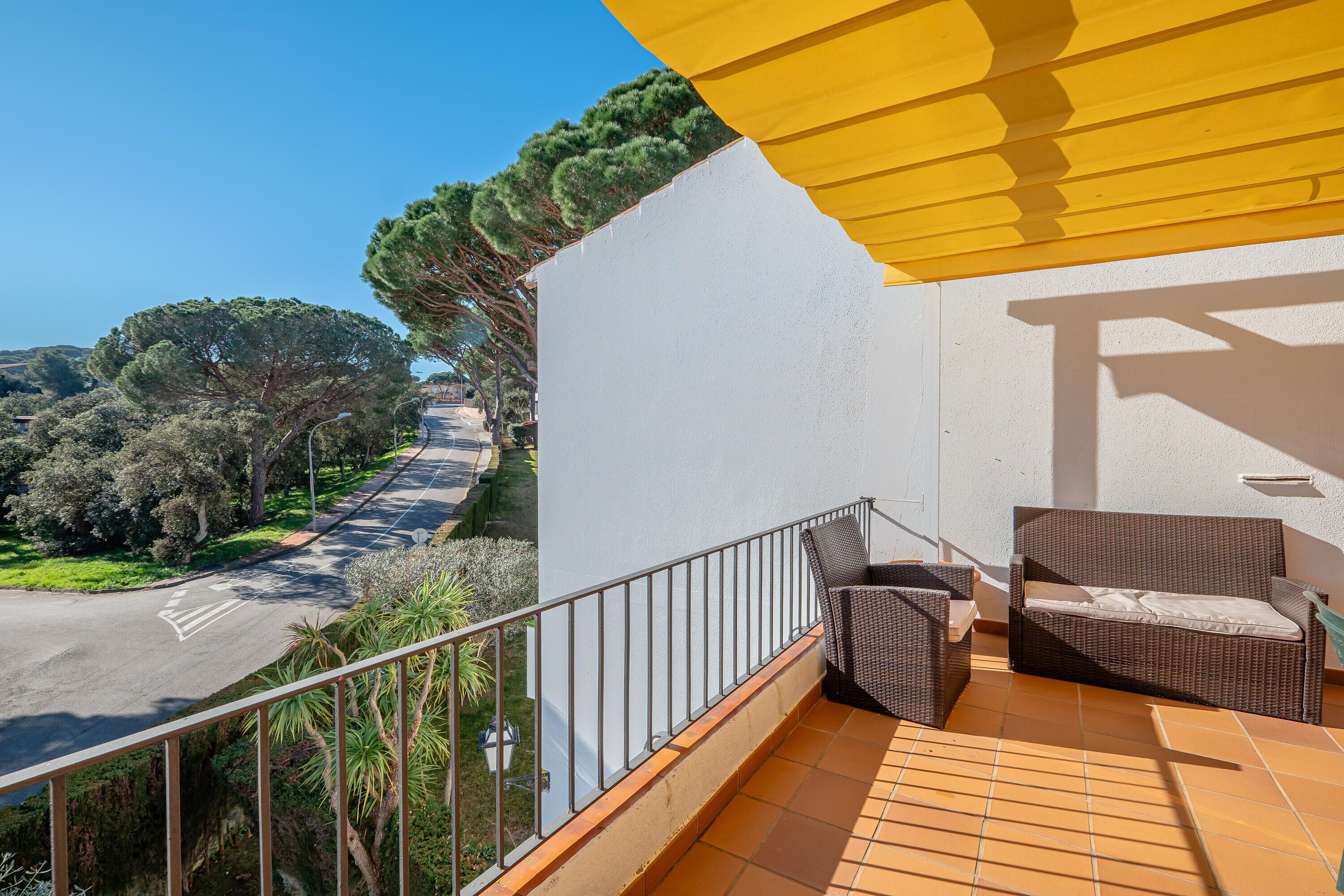A balcony with wicker furniture, a yellow awning, and a view of a road and trees.