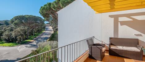 A balcony with wicker furniture, a yellow awning, and a view of a road and trees.