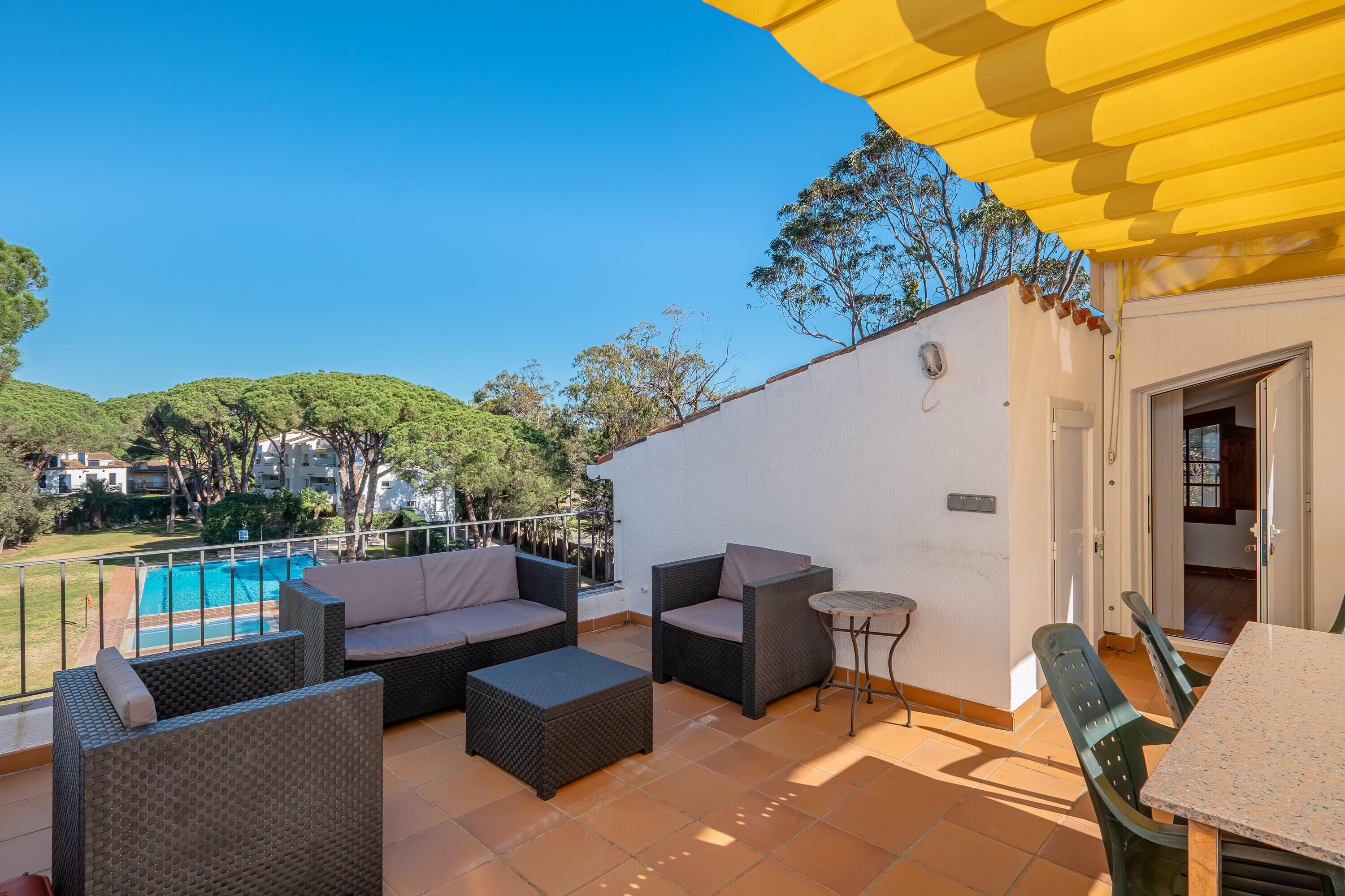 Un balcón con mobiliario de mimbre, una mesita y vistas a una piscina.