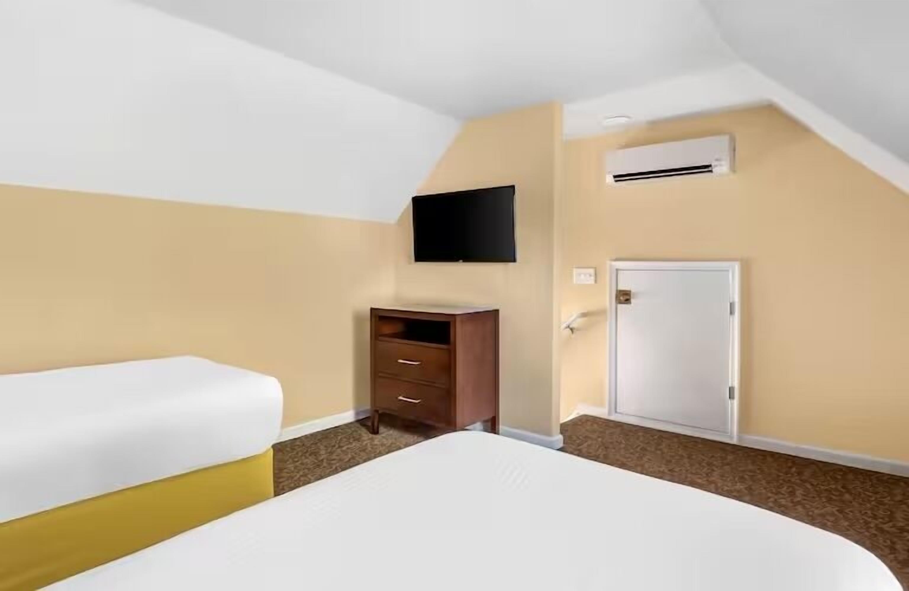 Een hotelkamer met een bed, een dressoir, een aan de muur bevestigde televisie en een airconditioning.