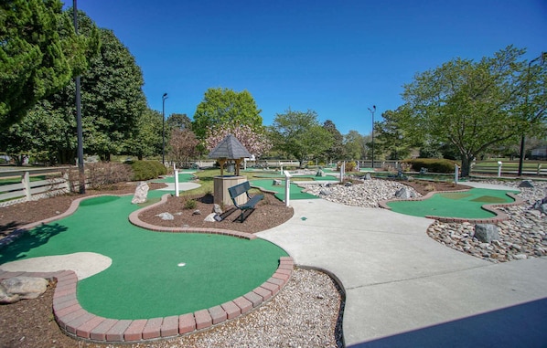 Un campo de minigolf con zonas de juego verdes, un pabellón y una banca.