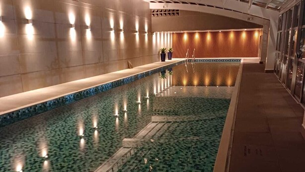 Una amplia piscina cubierta con piso de diseño de cuadros, rodeada de paredes con iluminación empotrada y paneles de madera.