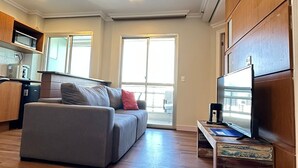 Una sala de estar moderna con un sofá gris, suelo de madera y un televisor de pantalla plana sobre un mueble de madera.
