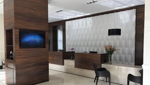 Zona de recepción de un hotel con un mostrador de madera, un televisor de pantalla plana y dos sillas negras.