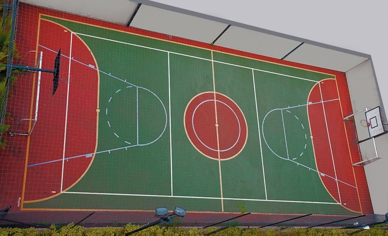 A basketball court with a red and green surface, white lines marking the court, and a basketball hoop on the right side.