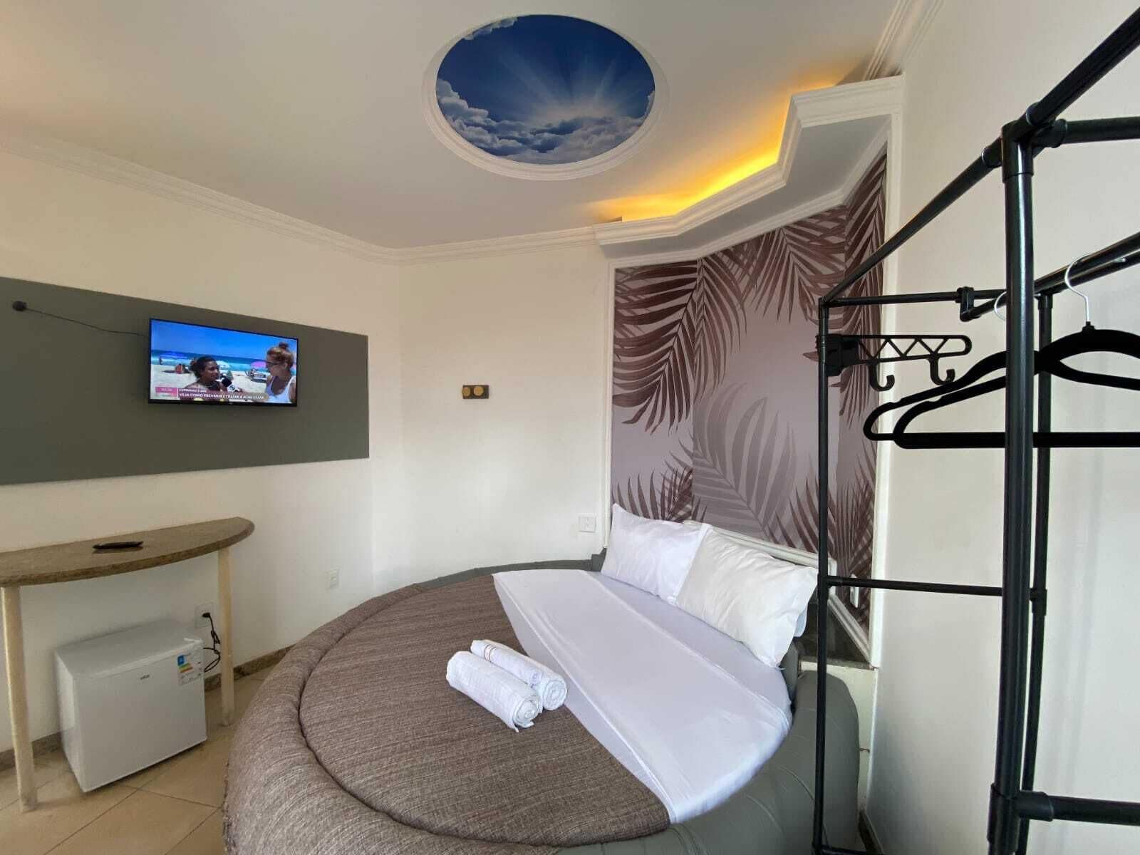 Un dormitorio moderno con una cama redonda, un televisor en la pared, un escritorio pequeño y un tragaluz circular en el techo.