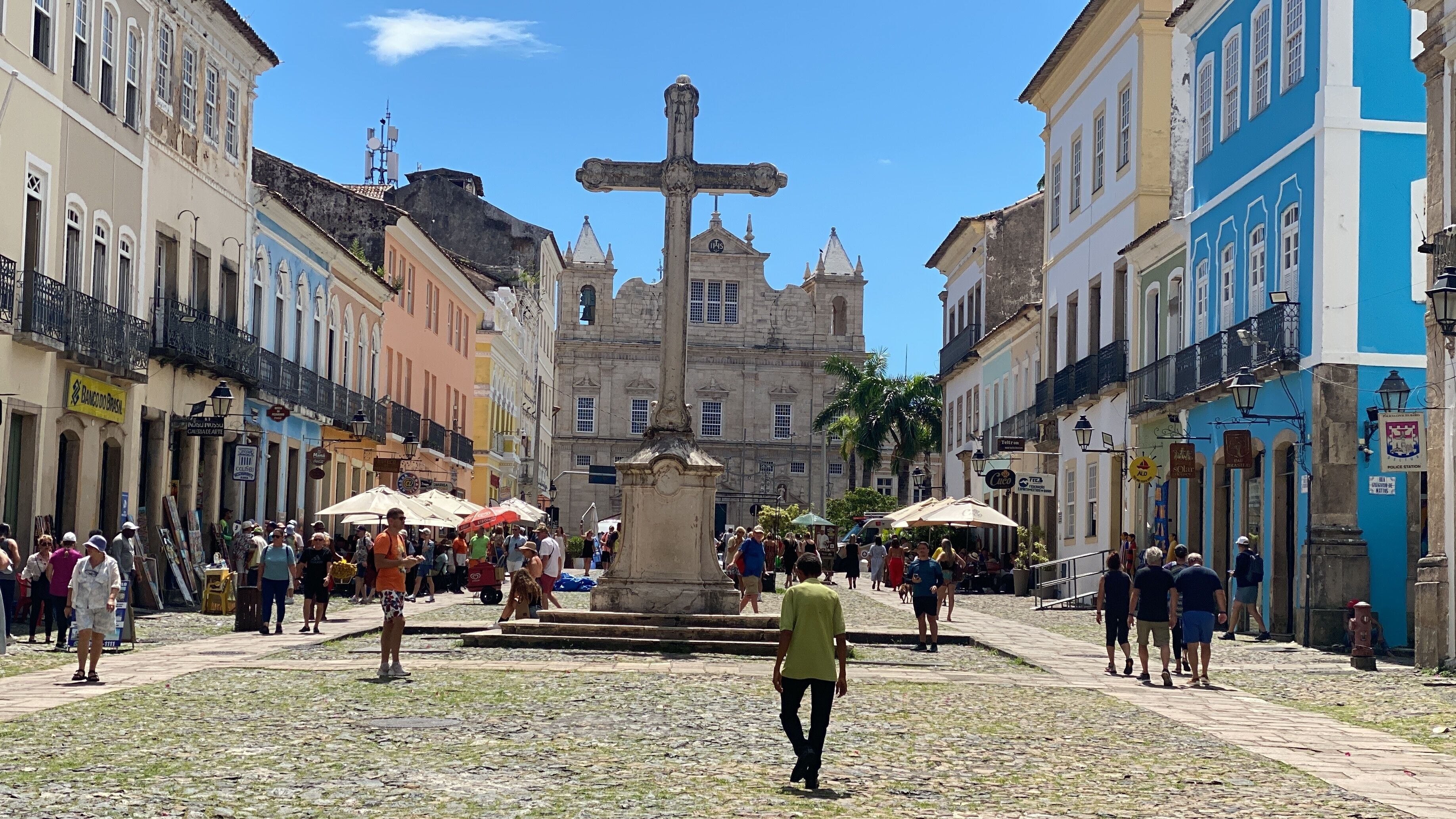 Uma praça de paralelepípedos com uma fonte central, rodeada por edifícios históricos com sacadas e placas.