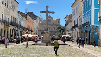 Uma praça de paralelepípedos com uma fonte central, rodeada por edifícios históricos com sacadas e placas.
