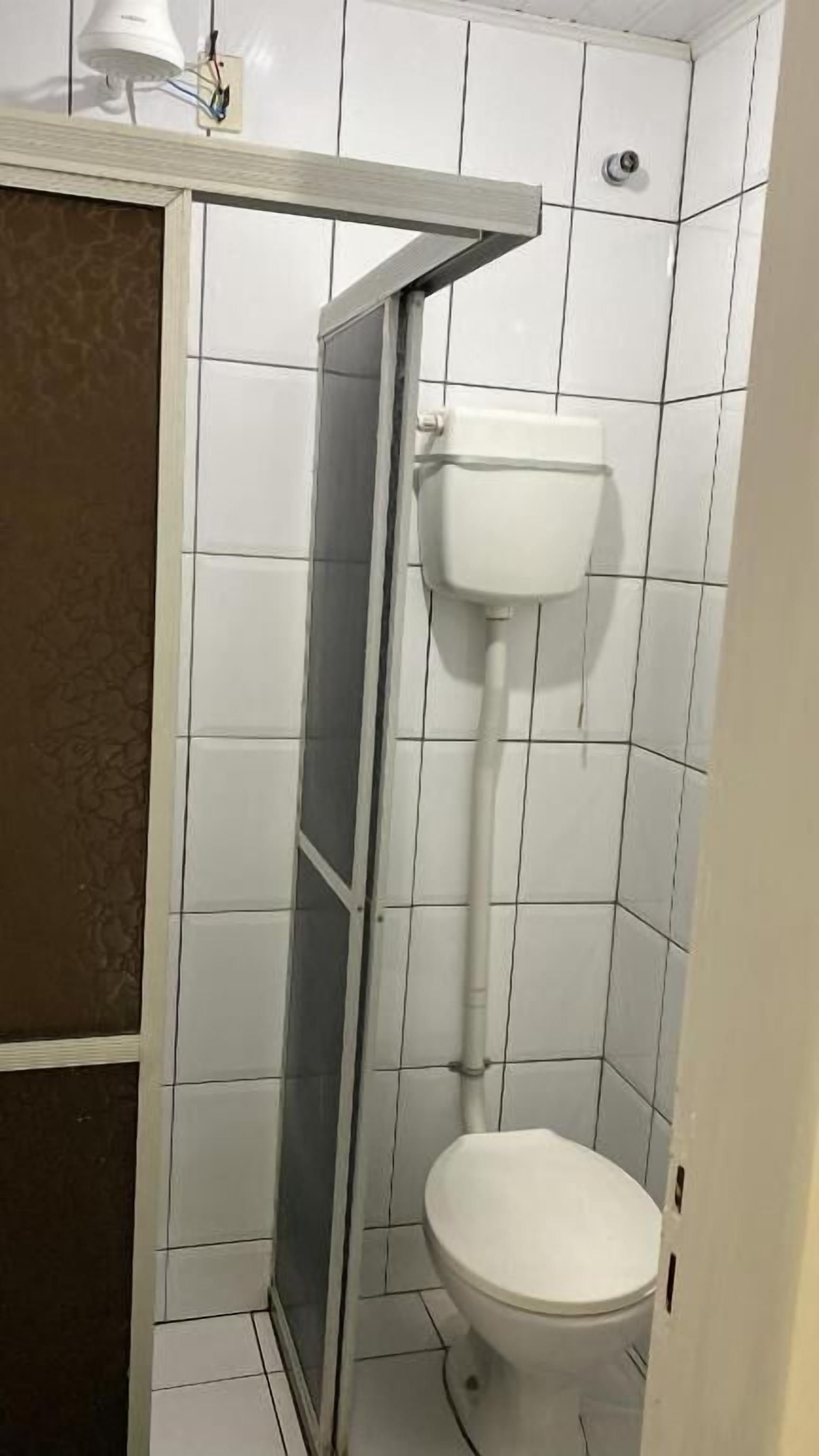 A small, tiled bathroom with a toilet, a shower enclosure, and a wall-mounted light fixture.