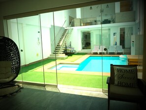 Un intérieur moderne avec une porte vitrée donnant sur un espace piscine, un escalier et un coin salon agrémenté d'un coussin orné de l'inscription « HOME Sweet HOME ».