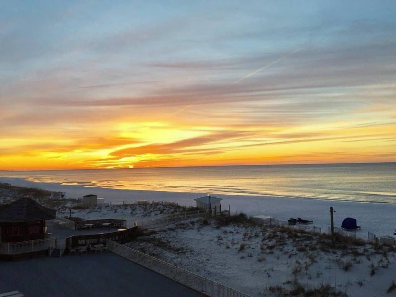 Vista a la playa con un atardecer, arena y un pequeño edificio con techo.