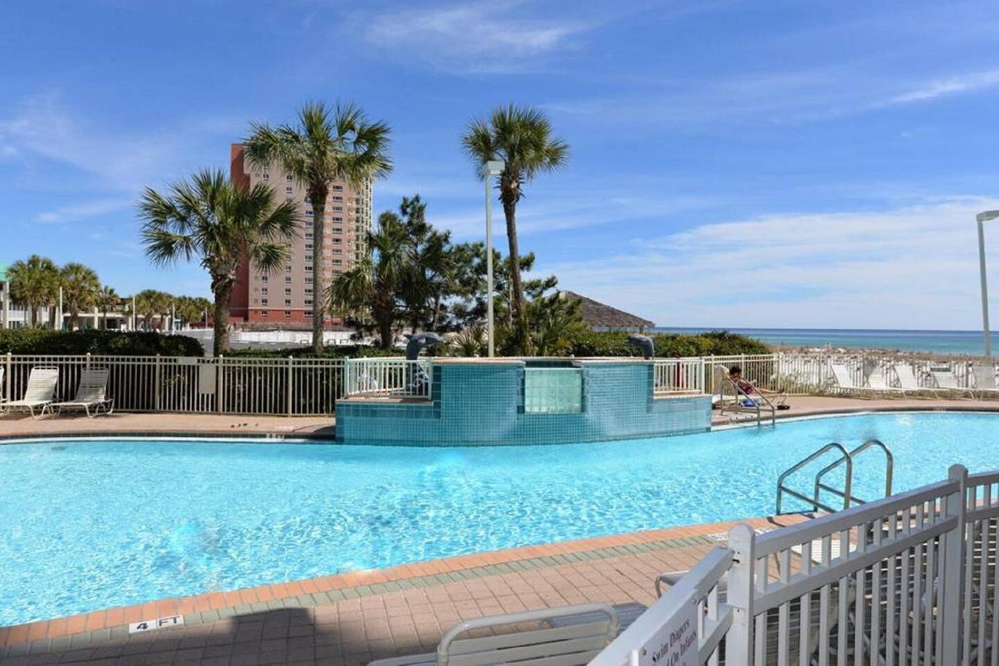 A swimming pool with a view of the ocean, surrounded by palm trees and a tall building in the background.
