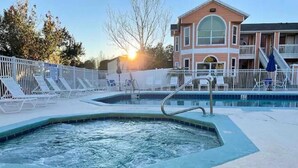 Una piscina con hidromasaje, sillas de descanso y un edificio con balcón al fondo.