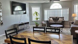 Un comedor con una mesa de madera en espiga y sillas negras, un ventilador de techo y un televisor montado en la pared.
